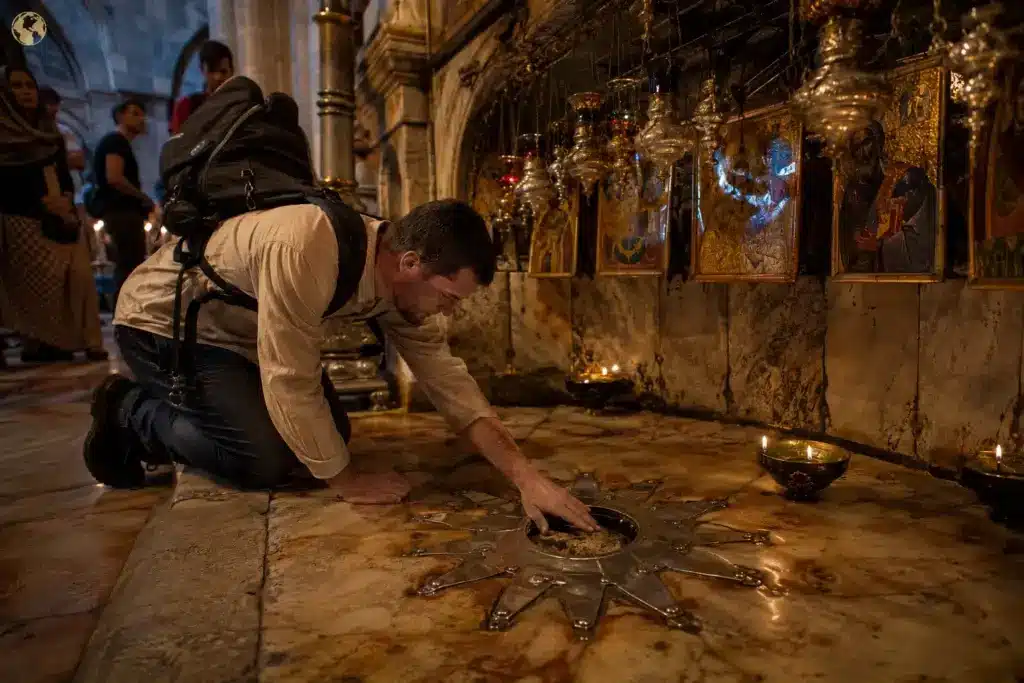 A pilgrim reaches through the silver disk beneath the Greek Orthodox altar to touch the exposed limestone of Golgotha inside the Church of the Holy Sepulchre in Jerusalem.